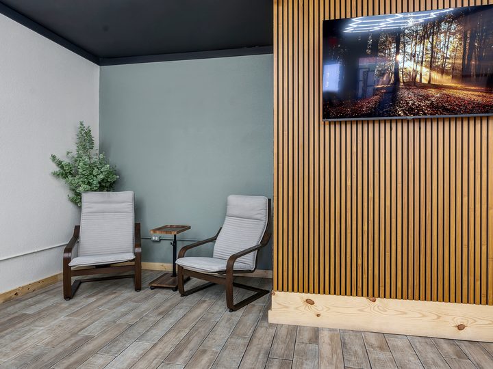 A quiet corner: two wood-framed chairs either side of a small round table against a pale green wall, beside a slatted wood wall carrying a wall-mounted screen.